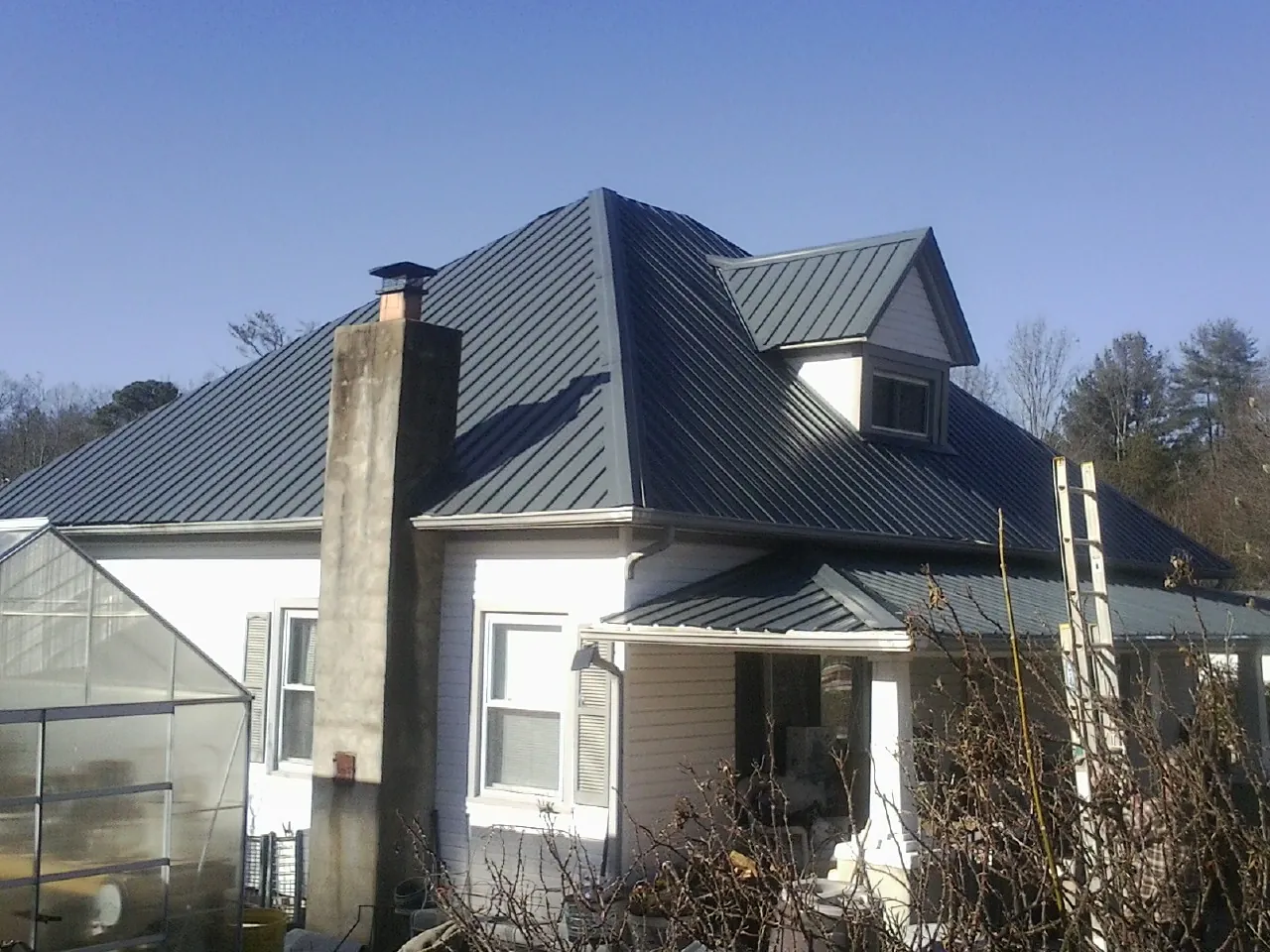 Dark blue standing seam metal roof on a white farmhouse with dormer — Slate & Tile Roof Repair by Roofing Brothers in Nemaha
