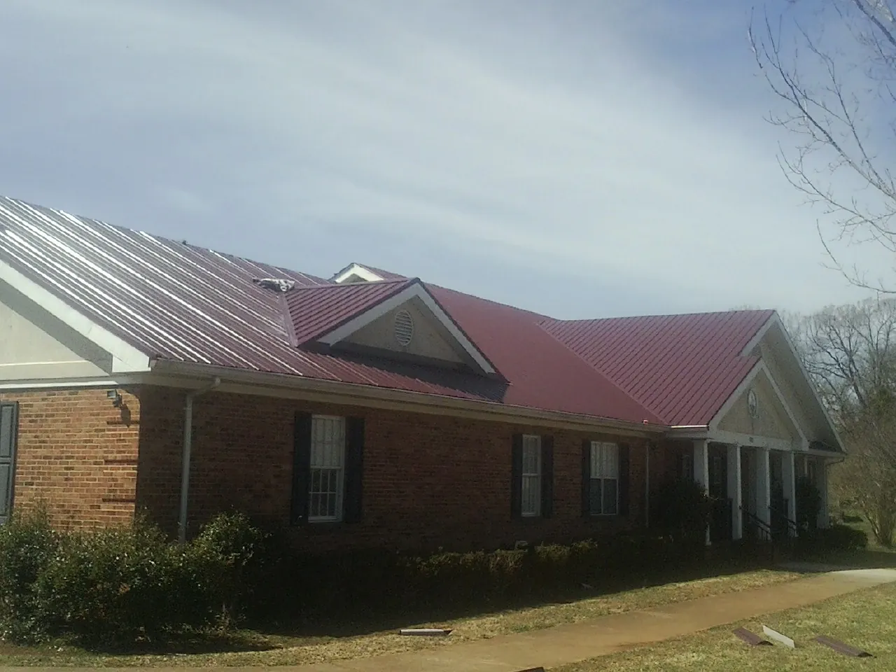 Red metal roof with gabled entries on a long brick building, from a Hail Damage Roof Repair job in Nemaha