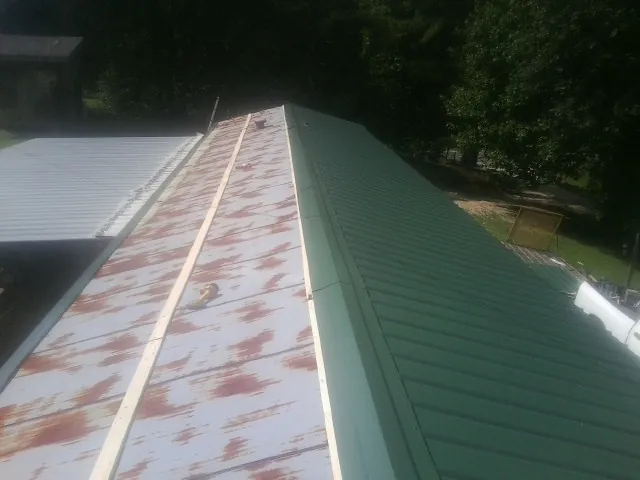 Old rusted panels beside newly installed green metal roofing — Wind Damage Roof Repair by Roofing Brothers in Nemaha