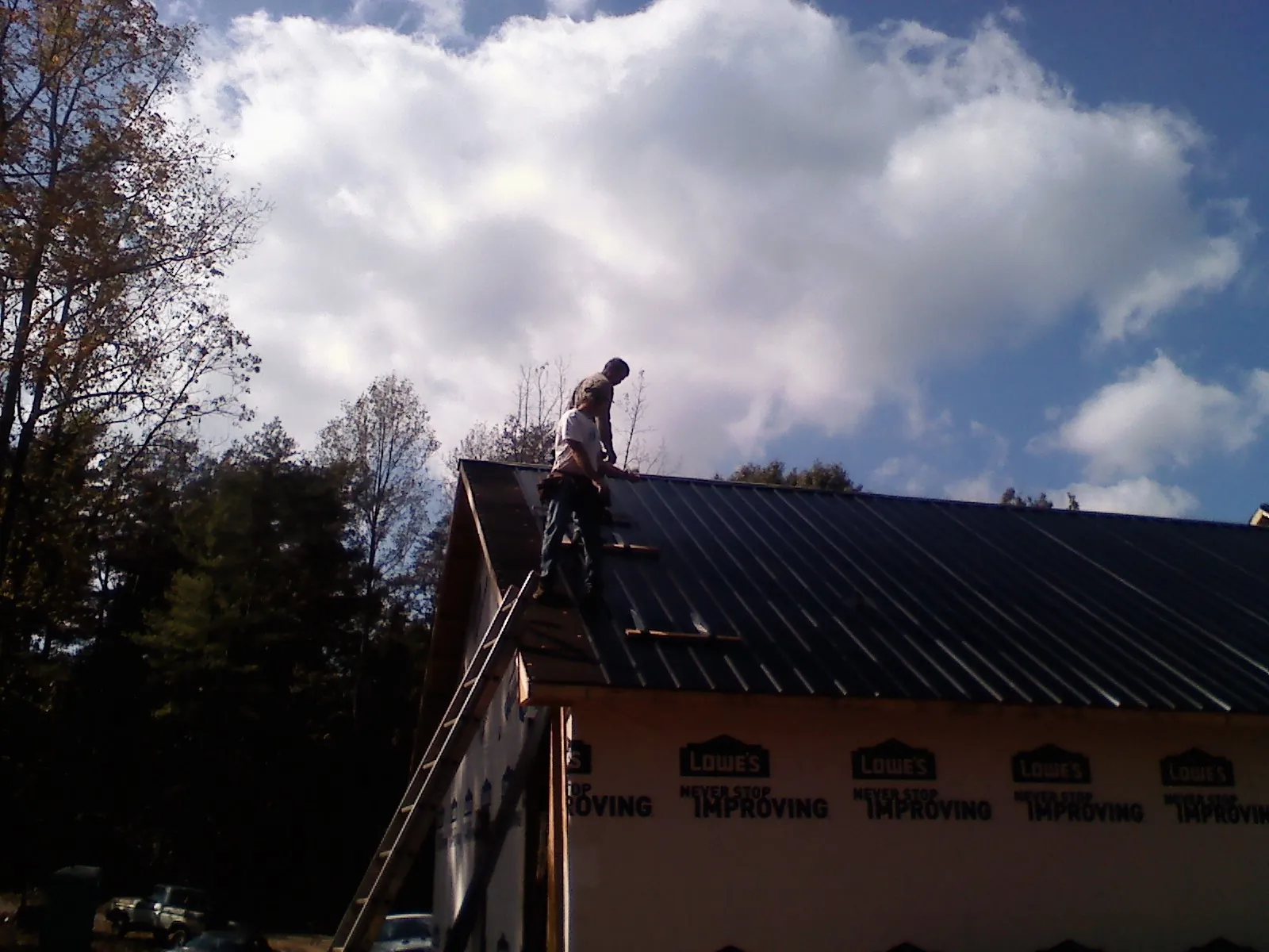 Roofer fastening dark metal panels high against a cloudy sky, from a Roof Inspection job in Nemaha