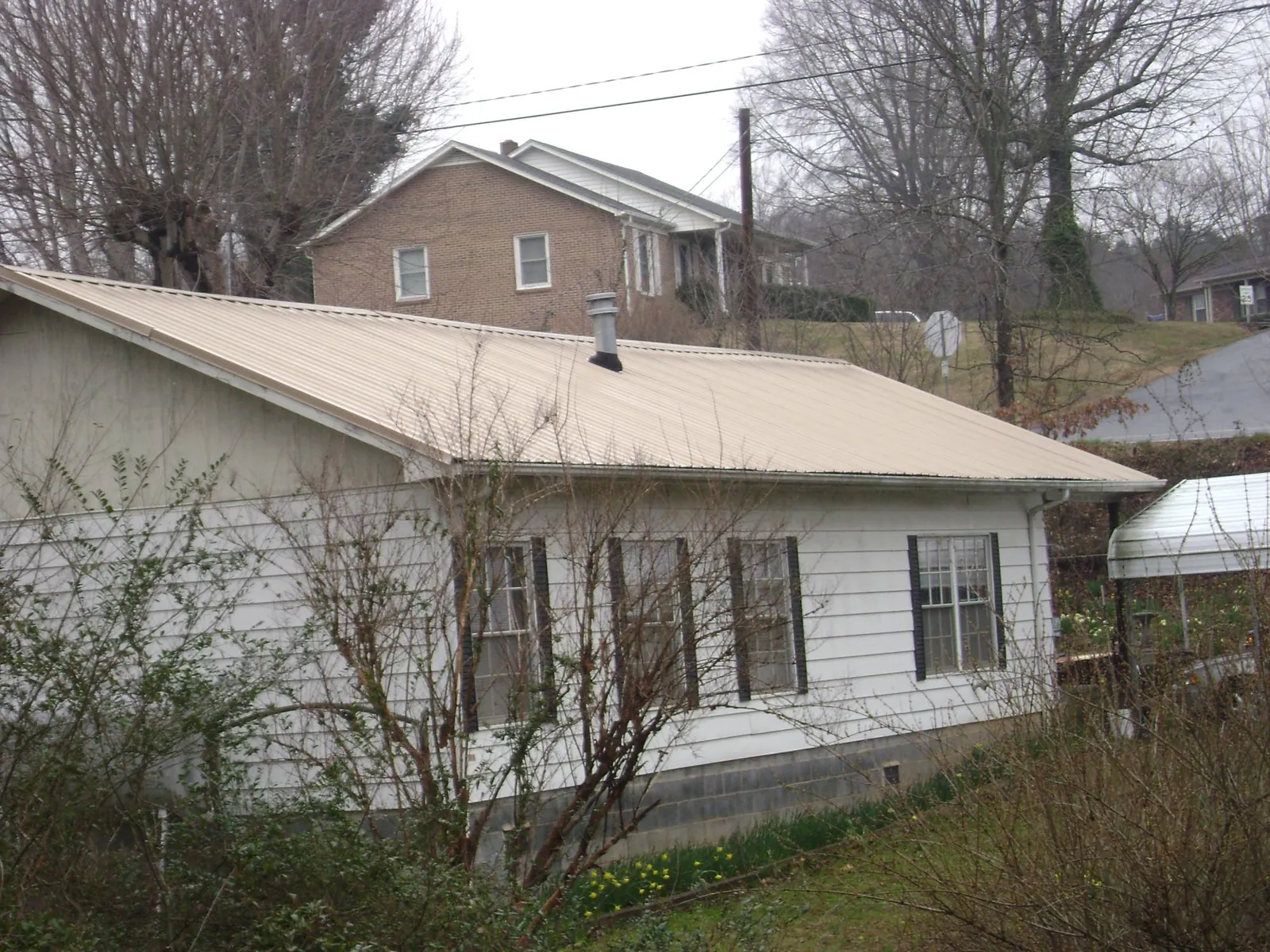 Tan metal roof on a white sided house set into a hillside — Commercial Roofing by Roofing Brothers in Nemaha